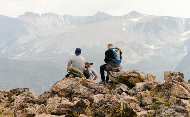 Hikers resting on a rocky summit with Colorado mountains behind them